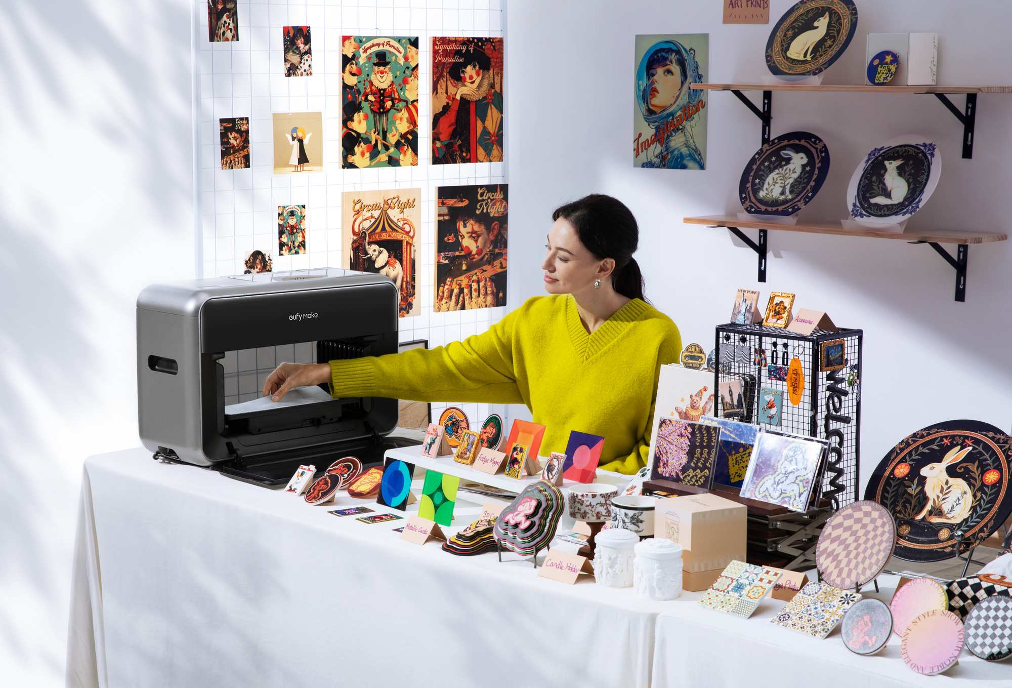 An operator loads the eufyMake E1 in a bright studio displaying colorful plaques, cards, coasters and decorative pieces.