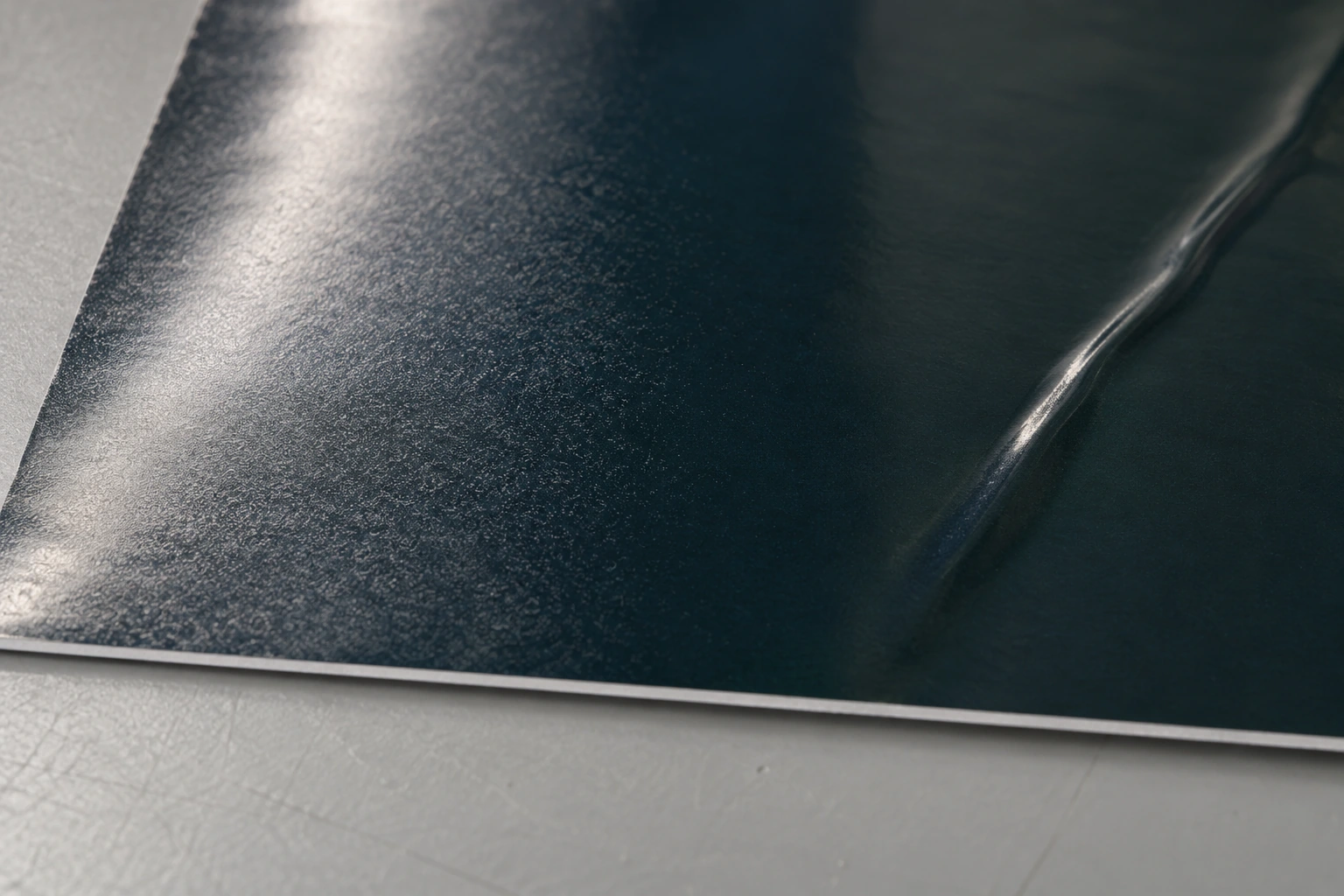 Illustrative macro of fine silvery haze at the left of dark laminated vinyl and a distinct shallow diagonal wrinkle at the right.
